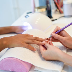 Close-up of beautician painting a woman's nails with a brush in a nail salon. Costumer receiving a manicure.